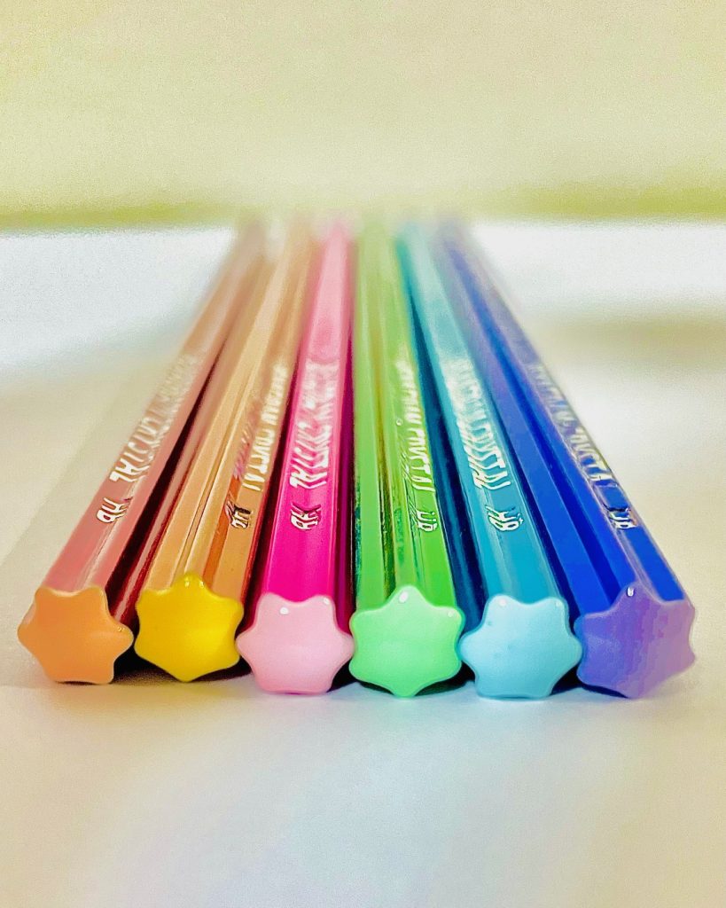 Pastel HEXAGRAMU CRYSTAL pencils arranged in a row, showing star-shaped ends in multiple colors.